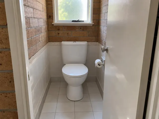Clean white toilet in a small tiled bathroom with brick walls and a window in St Marys