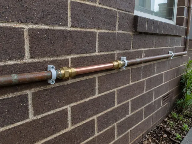 Repaired copper water pipe on a brick exterior wall beside a window in St Clair